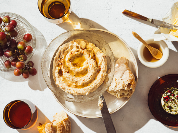 Ahorn-Bohnencreme mit Cashewnüssen mit Brot, Trauben und Getränken auf hellem Tisch angerichtet.
