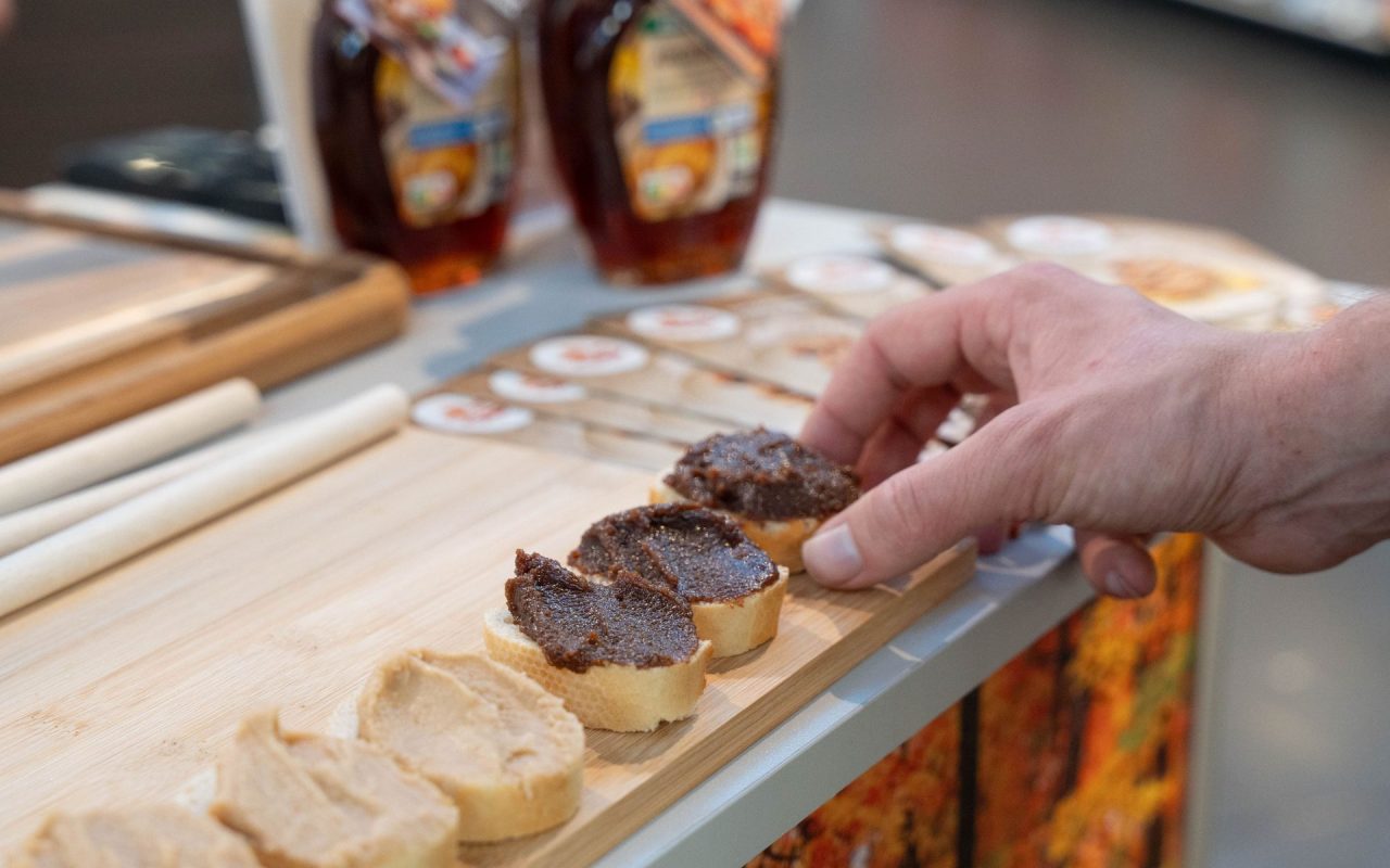 Brotscheiben mit Aufstrich. Hand greift nach Brotscheibe bestrichen mit Ahorn-Nuss Nougat Creme.